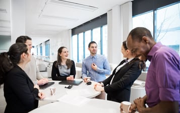 Mitarbeiter um einen Tisch stehend und lachend Mitarbeiter um einen Tisch stehend und lachend