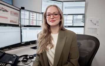 Kvinna sitter vid skrivbord och tittar in i kameran